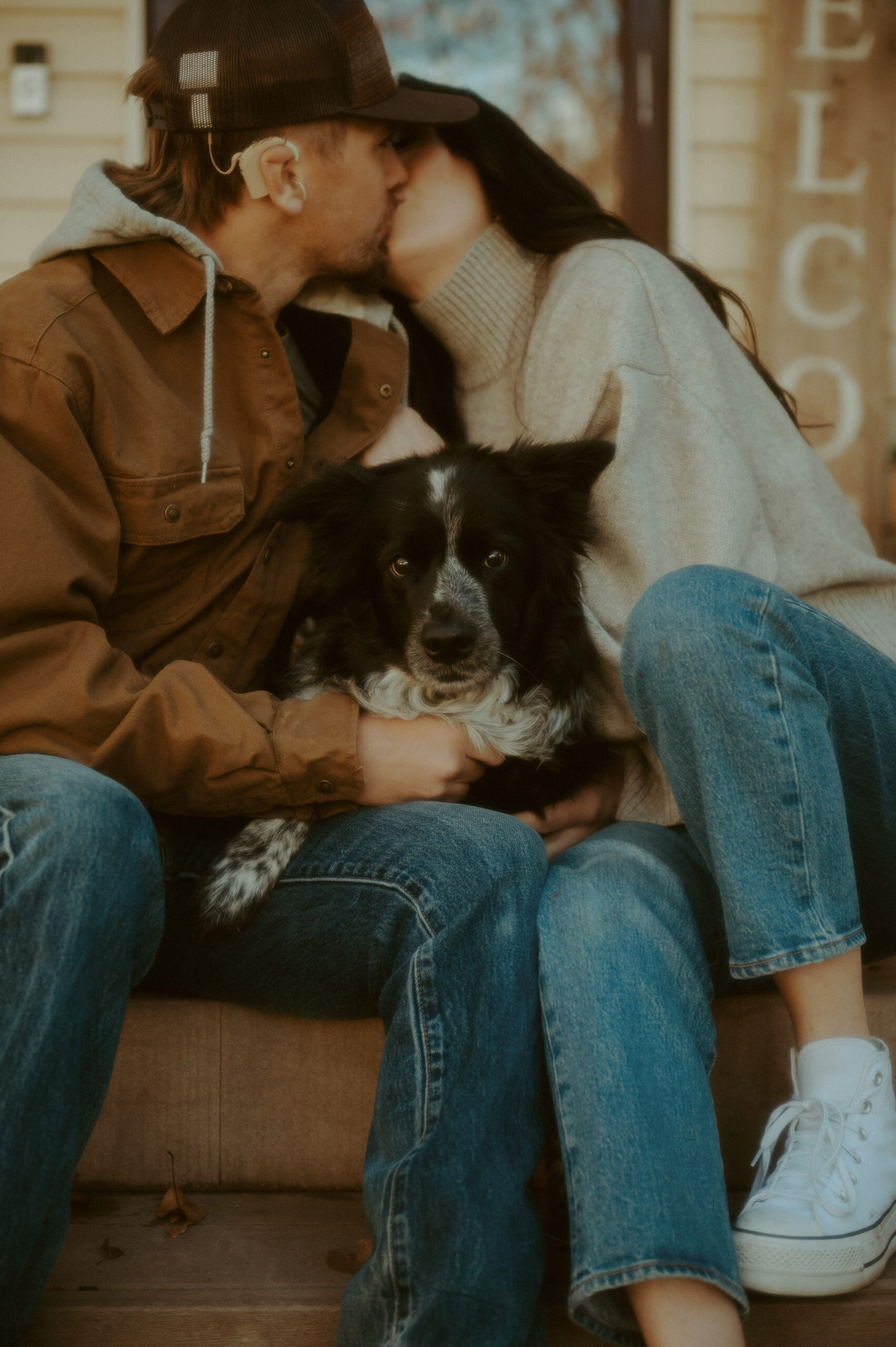 couple kissing and holding their dog during their at-home photography session